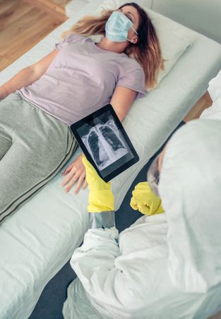 Doctor in protective suit examining x-ray of patient on tablet