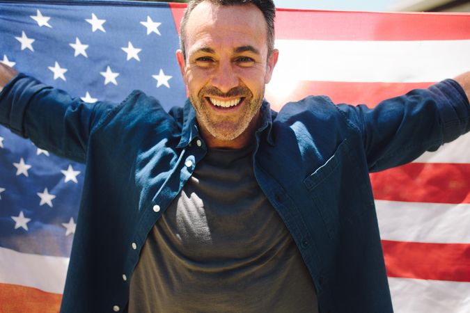 Close up of a smiling man holding American flag behind him