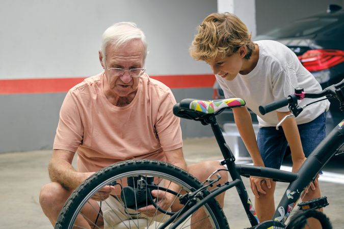 Mature man checking bicycle tire pressure with grandson