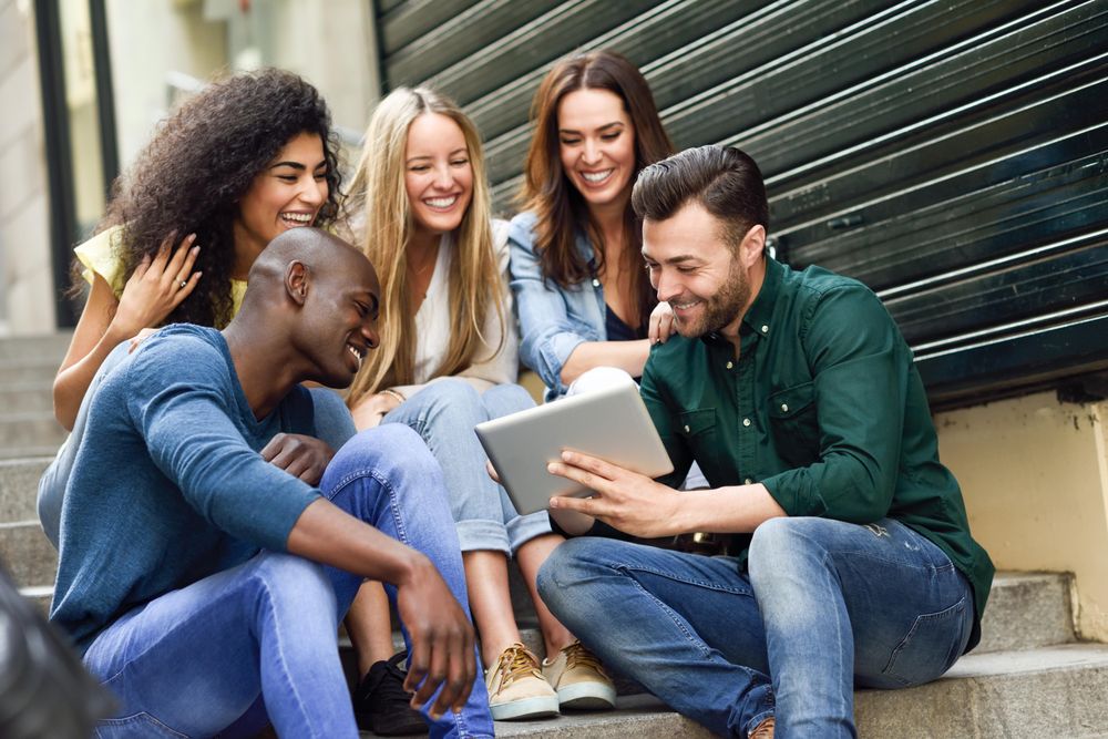 Friends entertained by something on digital tablet while sitting on outdoor cement staircase