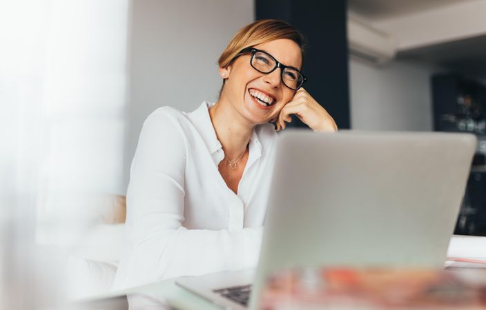 Smiling business woman in spectacles sitting at her desk in office