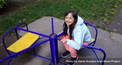 Little girl sitting on playground equipment in play clothes smiling and looking up at camera 0LYXA5