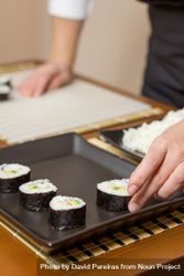 Chef placing Japanese sushi rolls with rice, avocado and shrimps in nori seaweed sheet over a rectangular tray 5rdnMb