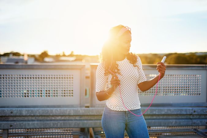 Woman listening to music with pink head phones on sunny rooftop