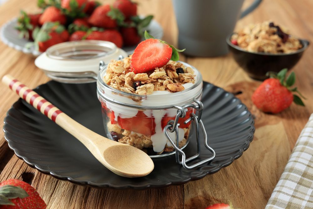 Pot of Greek yogurt parfait with strawberries and granola served with spoon