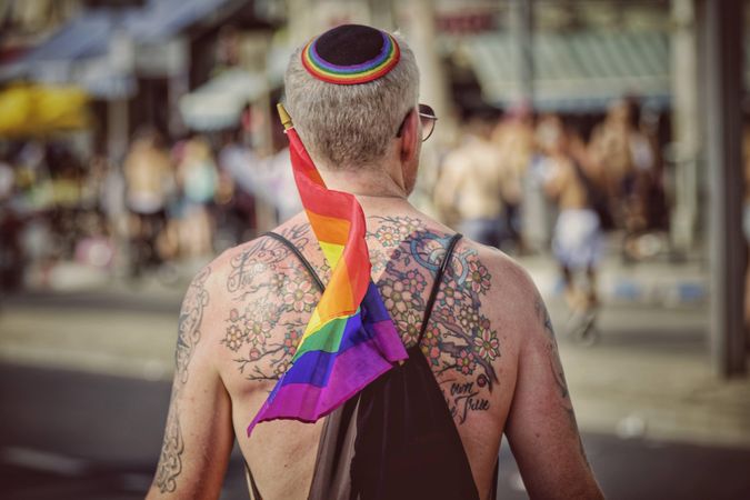 Backside of man with tattoos on his back and rainbow flag in his backpack