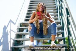 Laughing female skater checking phone on stairs 5aQyP5