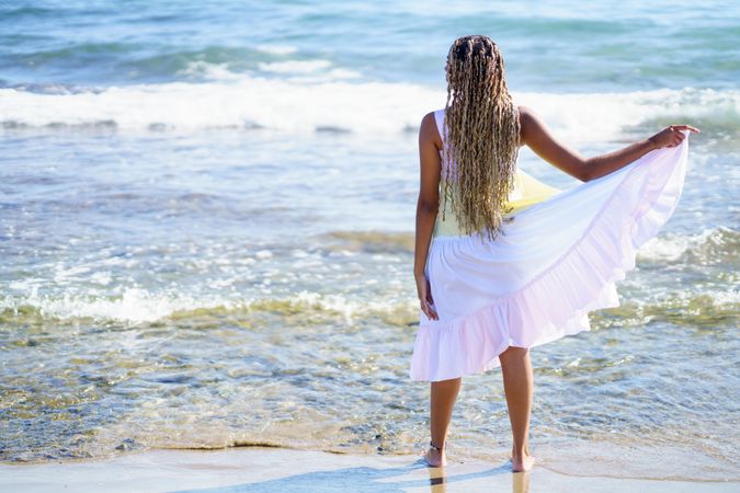 Barefoot Black woman walking along the coast in colorful dress