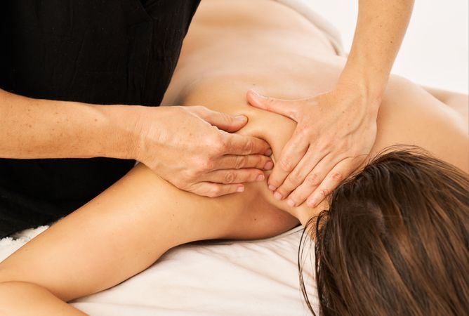 A masseuse massaging the shoulder of a woman with shoulder