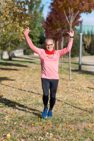 Happy grey haired man running in park with arms up