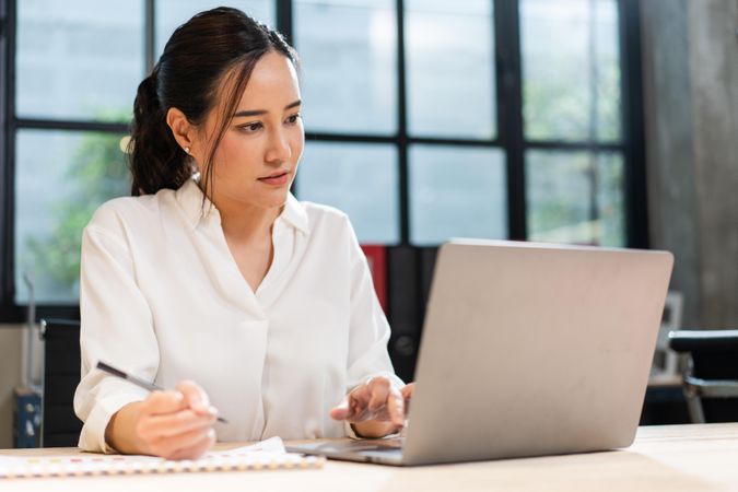 Woman writing notes from laptop in office