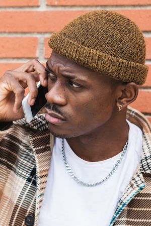 Black male speaking on smartphone near brick wall