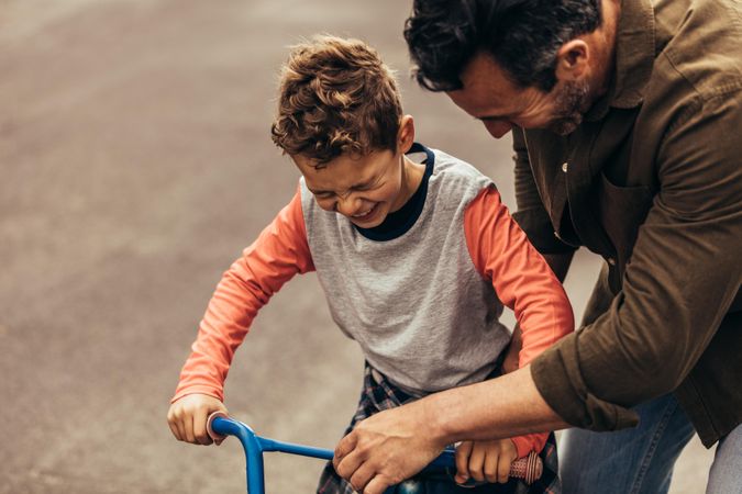 Father and son laughing together while child is sitting on bike