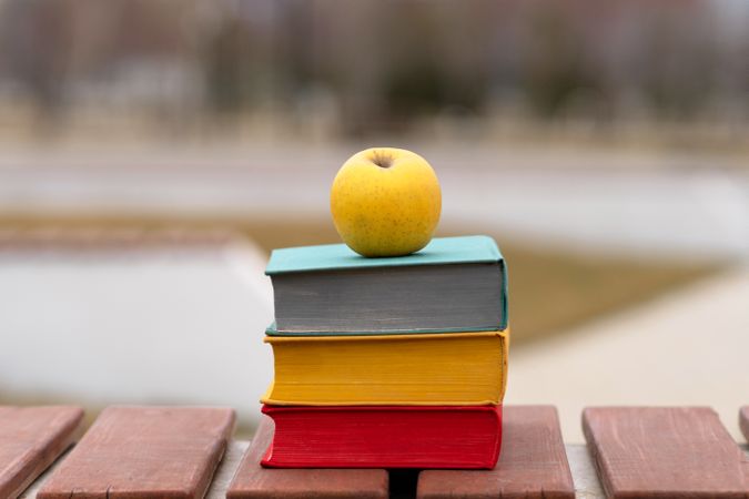 Single yellow apple placed atop stack of hardcover books.