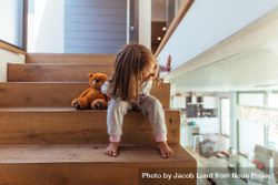 Cute little girl sitting on staircase and looking down through a glass wall indoors 43QrO0