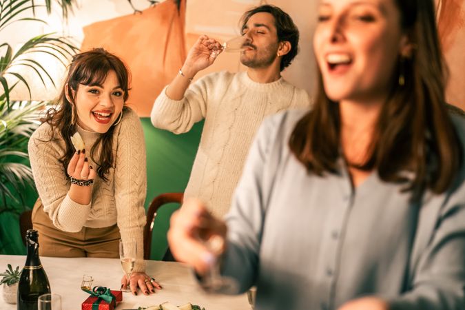 Happy young woman eating an appetizer and smiling at a Christmas party with friends.