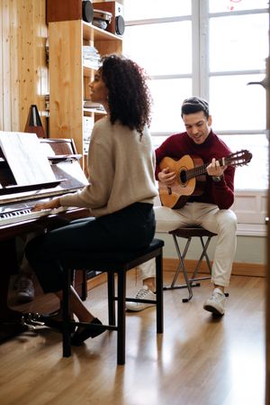 Woman playing piano near man playing guitar in studio