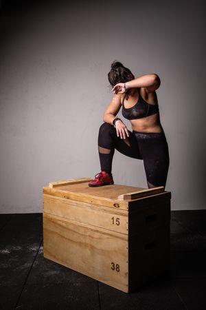 Woman jumping on wooden box in gym