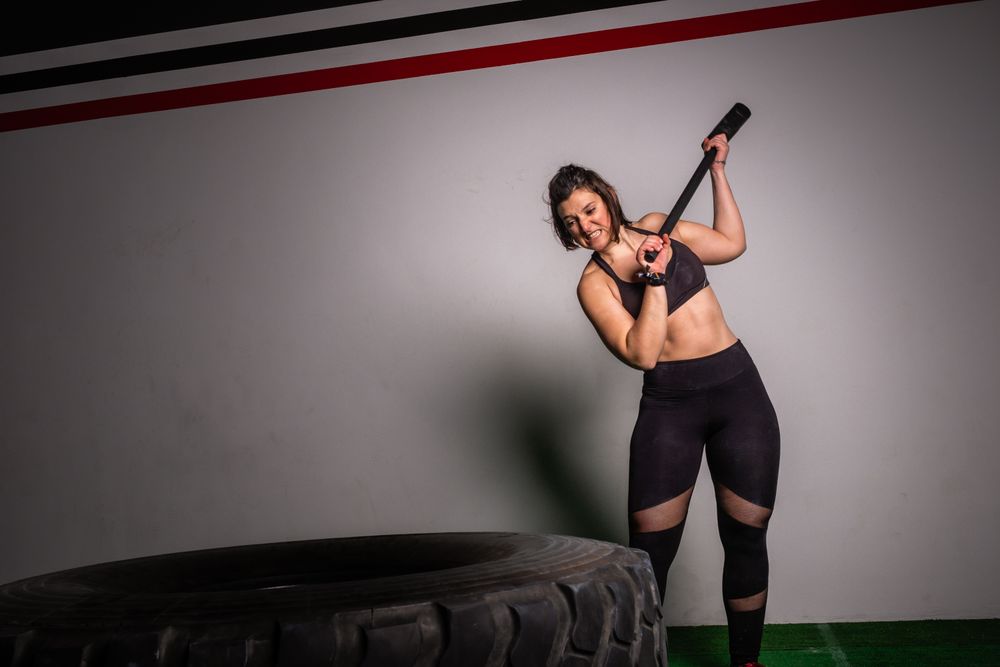 woman with hammer hitting on tire in gym