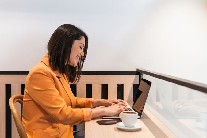 Cheerful woman typing on laptop and working in cafe