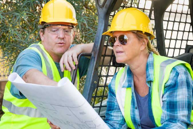 Male and Female Workers With Technical Blueprints Talking at Construction Site