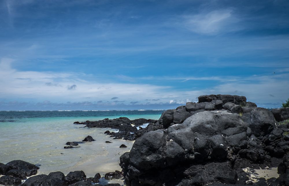 Dark lava rocks on the beach before the crystal waters of the Indian Ocean