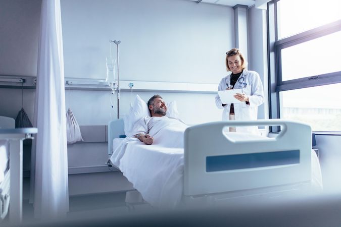 Female doctor talking to male patient in hospital bed