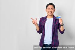 Asian male in grey studio with pointing to the side with credit card 42KQKb