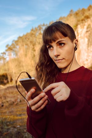 Young woman with piercing listening music on smartphone on hill