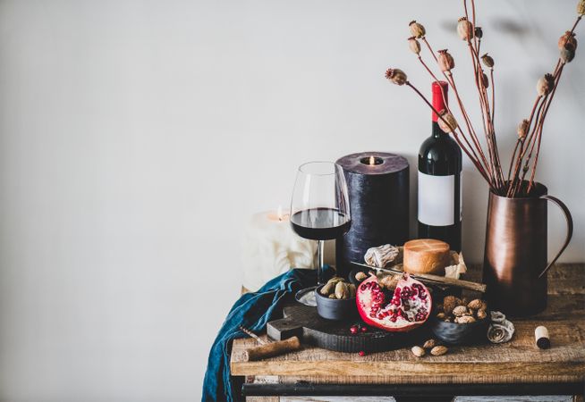 Rustic setting of wine, cheese, candle, with pomegranate, and dried poppies, with copy space