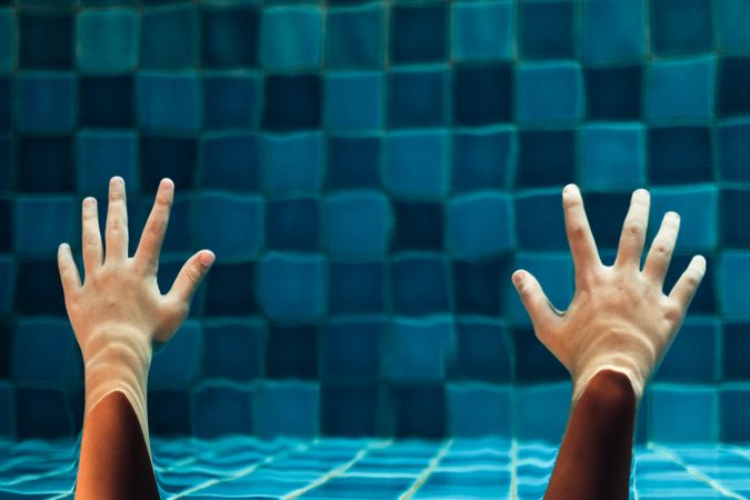 Two hands reaching out under water in a pool