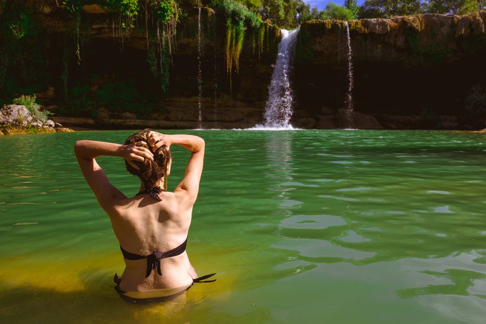Anonymous woman touching hair and looking at waterfall