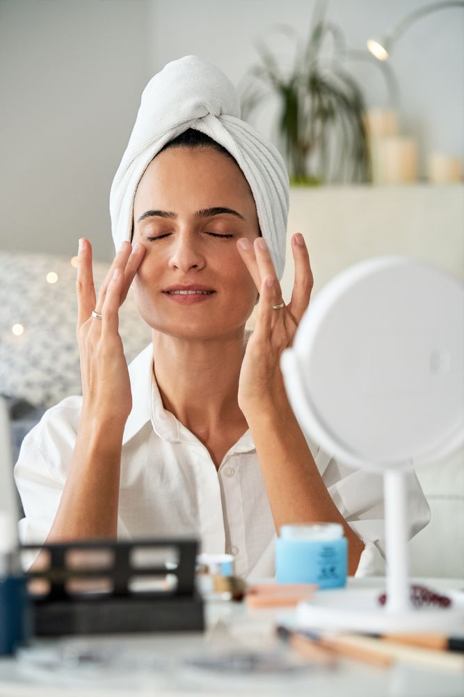 Delighted woman smearing anti aging cream under eyes