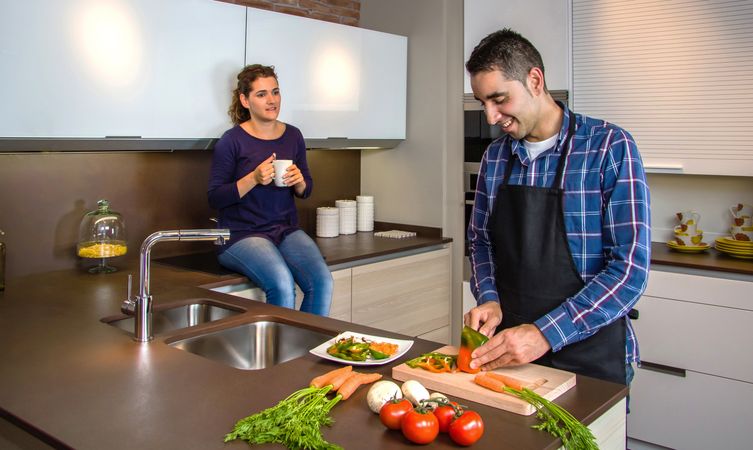 Couple chatting in the kitchen while the husband cuts vegetables to prepare food