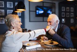 Older man kissing hand of smiling woman at restaurant date bYMlGb