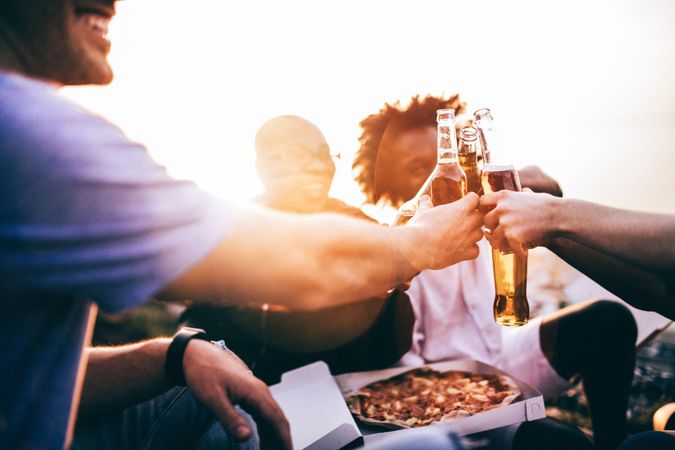 Group of friends toasting over beers, and pizza at sunset