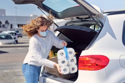 Young woman in mask placing purchases in car trunk