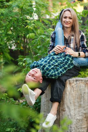 Portrait of young mother spending time with son on tree stump