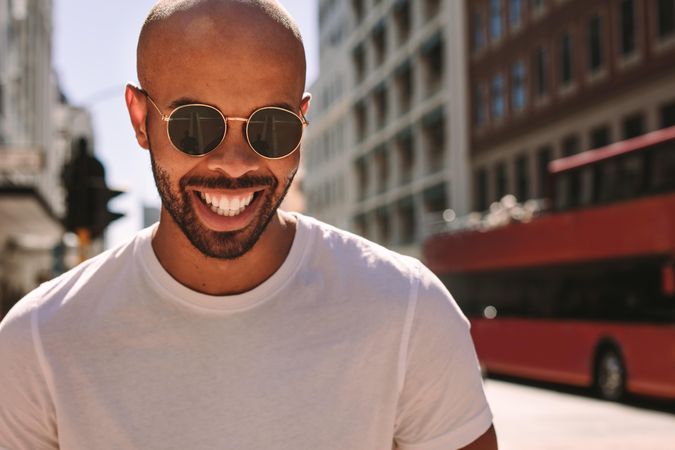 Close up portrait of handsome young man wearing sunglasses walking down the street and smiling