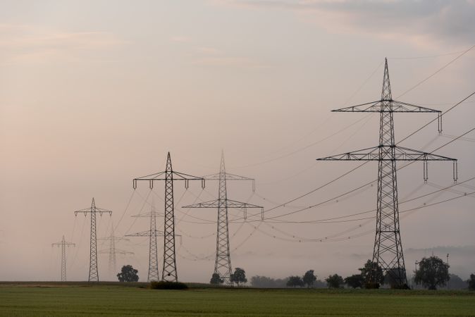 Electricity pylons in a row over the agricultural fields on a foggy morning