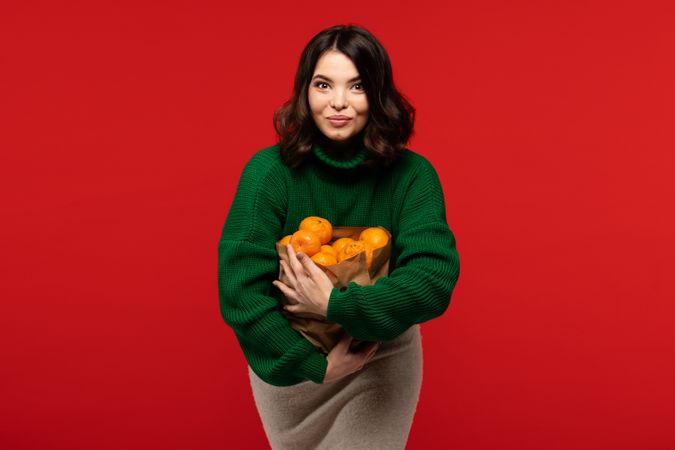 Woman making funny expression while holding bag of fresh tangerines