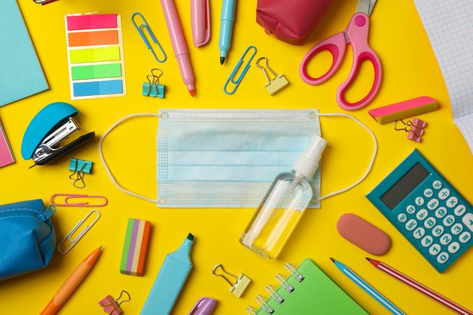 School supplies with medical mask and sanitizer on yellow background