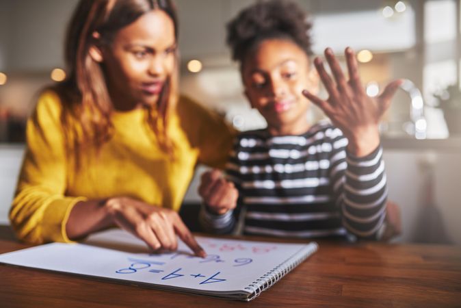 Daughter counting numbers on fingers while doing homework with mother