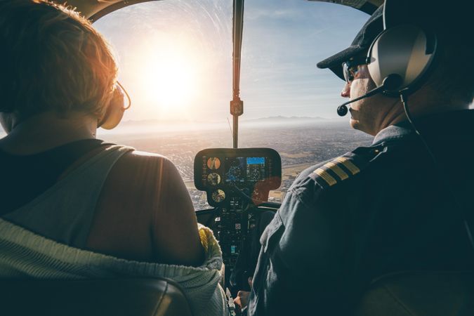 Rear view of male and female pilots flying a helicopter on sunny day