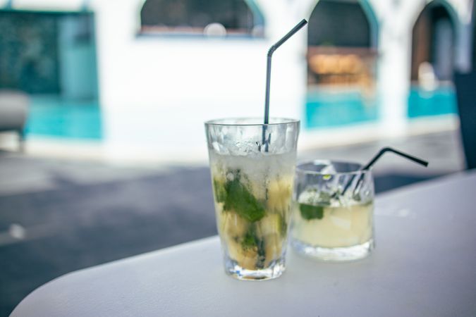 Two cocktails with straws on a table near a pool