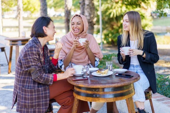 Three laughing women enjoying coffee and baked goods on a beautiful sunny day