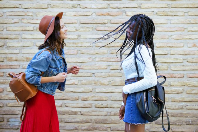 Two women facing each other and smiling beside a brick wall