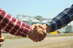 Businessmen shake hands against silos. Agriculture business
