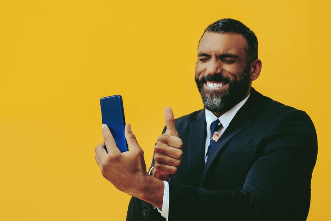 Smiling Black businessman in suit speaking at smartphone screen while giving the thumbs up