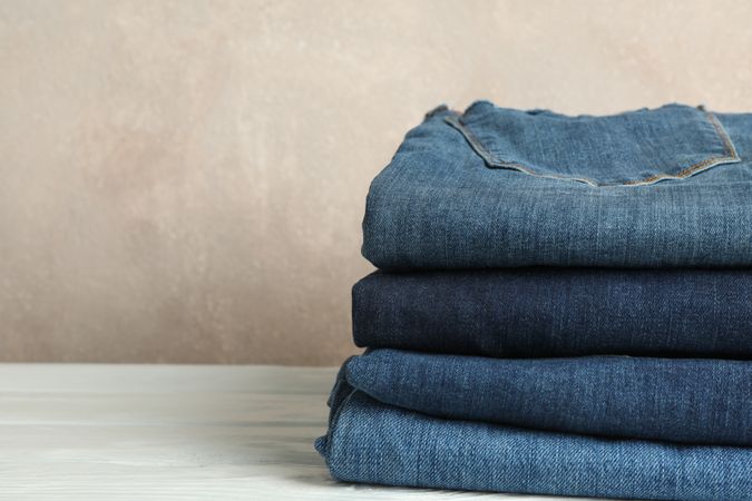 Stack of jeans pants on light background, space for text